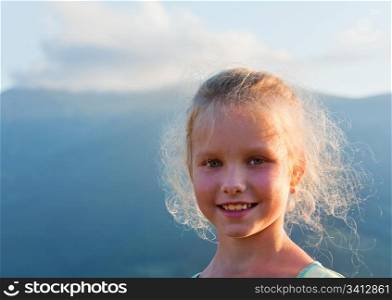 Small girl outdoor portrait in last sunset sunlight and summer mountain behind