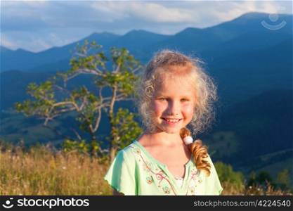 Small girl outdoor portrait in last sunset sunlight and summer mountain behind