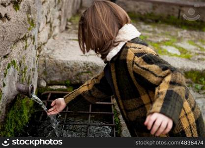 Small girl touching water from a natural fountain