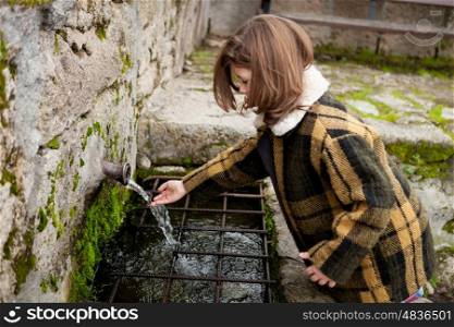 Small girl touching water from a natural fountain