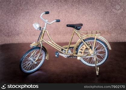 Small gold color toy bicycle on brown leather cushion