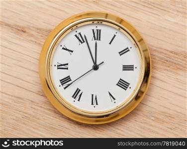 Small gold colored clock almost at midnight and laying on a wooden table