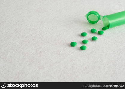 Small green pills with a little green pill bottle isolated against a white background