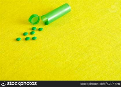 Small green pills with a little green pill bottle isolated against a yellow background