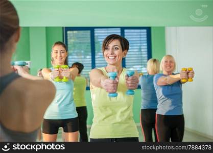 Small group of women are doing exercises with the dumbbell in the fitness studio