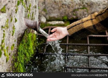 Small hand of a girl touching water from a natural fountain