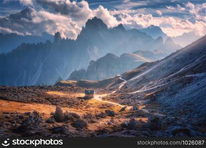 Small house in beautiful mountain valley, orange grass, stones, blue sky with clouds at sunset in autumn. Colorful landscape with building, mountains. Tre Cime park in Dolomites, Italy. Alps in fall. Small house in beautiful mountain valley and dramatic sky
