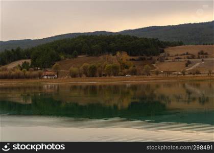 Small house with mountains, trees, vegetation and blue sky in the background, and a beautiful reflection on the lake in front of it