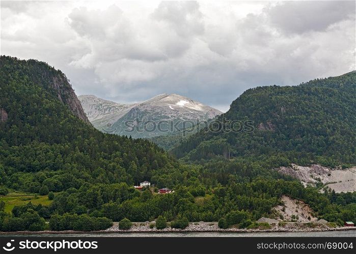 Small houses in the mountains along the Romsdalsfjorden near Andalsnes under a cloudy sky, Norway. Along the Romsdalsfjorden near Andalsnes, Norway