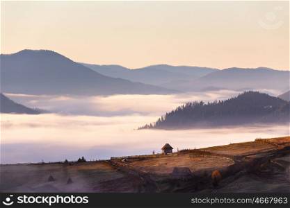 Small hut on mountain pass in autumn foggy morning. Mountain village and old farm in the mountains. Clouds of fog and sky at background