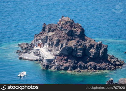 Small island of Saint Nicholas below village of Oia on Santorini. Island of St Nicholas in Oia