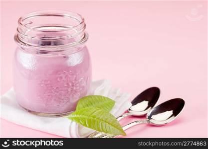 small jars with yogurt on rose background with leaves