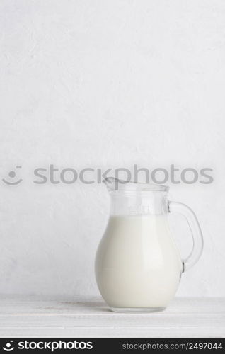 Small jug of milk on white wooden table vertical with copy space
