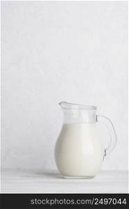 Small jug of milk on white wooden table vertical with copy space
