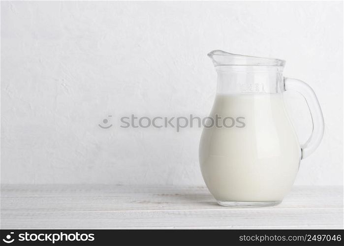 Small jug of milk on white wooden table with copy space