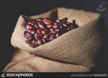 Small jute sack containing coffee beans on black background