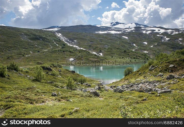 small lake in nature norway near gamle strynefjellsveg with blue water and mountains with snow in background