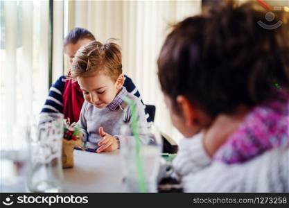 Small little boy caucasian child son sitting in the lap of his mother or aunt while female friend is looking at them teasing smiling holding smart mobile phone playing games making video call family