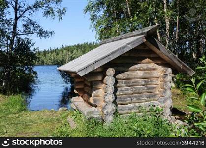 Small log cabin on the shore of forest lake, sunny summer day