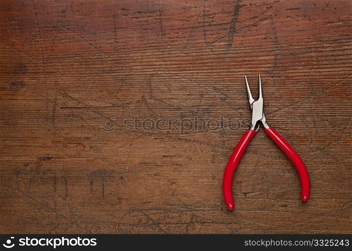 small needle nose pliers on a scratched and weathered wood background
