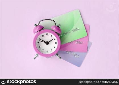 Small pink alarm clock lies on colored credit cards. The concept of modern fast online banking and funds transfer operations. Modern fast online banking and funds transfer operations
