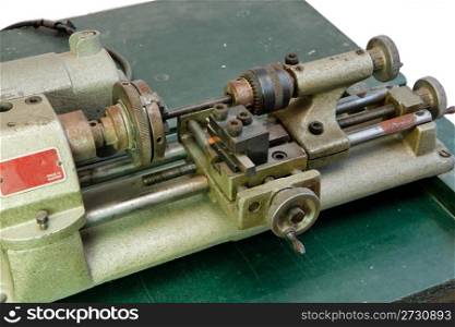 Small portable metal lathe on green board isolated closeup