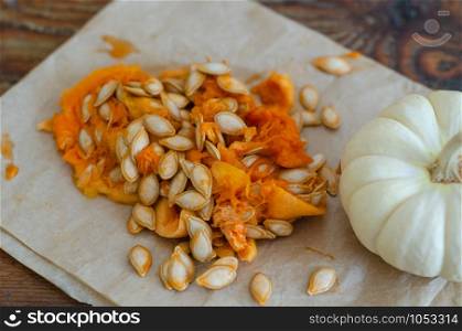 Small pumpkin and pumpkin seeds are on the wooden table.