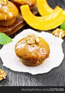 Small pumpkin cupcake with orange glaze and walnuts on paper, sprigs of mint on a wooden board background