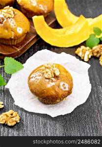 Small pumpkin cupcake with orange glaze and walnuts on paper, sprigs of mint on a dark wooden board background