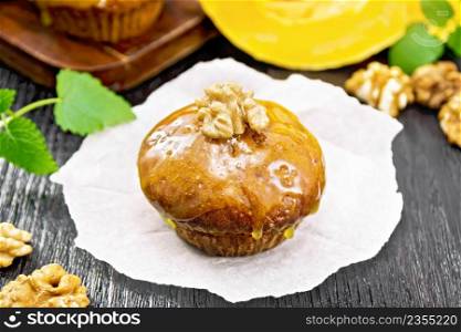Small pumpkin cupcake with orange glaze and walnuts on parchment, sprigs of mint on a dark wooden board background