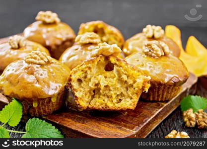 Small pumpkin cupcakes with orange glaze and walnuts, mint sprigs on a dark wooden board background