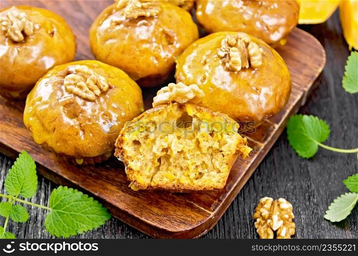 Small pumpkin cupcakes with orange glaze and walnuts, mint sprigs on a wooden board background