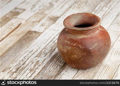 small red and brown clay plant pot (mass produced planter) with rough, grunge finish, on white wood background