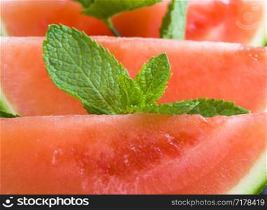 small red and juicy watermelon on a wooden board, sliced with slices of berries with leaves of green and fragrant mint. watermelon on a wooden board