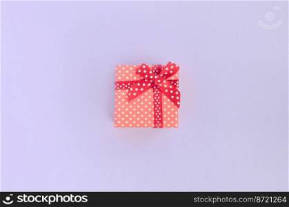 Small red gift box with ribbon lies on a violet background. Minimalism flat lay top view.. Small red gift box with ribbon lies on a violet background. Minimalism flat lay top view