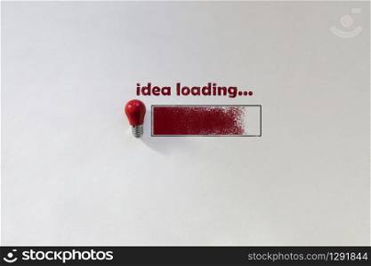 Small red light bulb top view on white background. Chalk inscription Idea loading and drawn loading bar. Concept thought arising. Top view picture with copy space