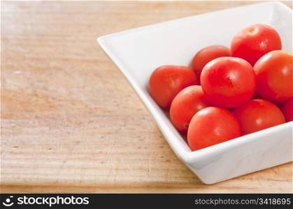 Small red tomatoes sit in a modern white bowl on timber