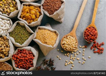 Small sacks with various dried fruit and cereals packed. Two wooden spoons on grey background. Healthy legumes and grains