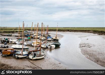 Small sail boats moored at Blakeney Harbour in Norfolk during low tide on a cloudy Summer day.