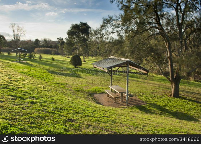 Small shelter in green parkland with seats and a table