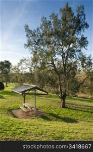 Small shelter in green parkland with seats and a table