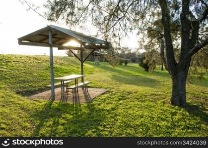 Small shelter in green parkland with seats and a table
