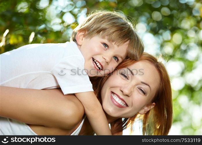 Small son piggyback on mother in a summer garden
