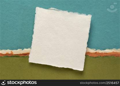 small square sheet of blank white Khadi paper against colorful abstract paper landscape