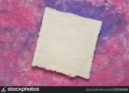 small square sheet of blank white Khadi paper against purple and pink marbled paper