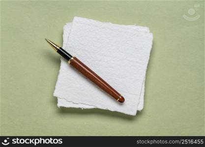 small square sheet of blank white Khadi paper with a stylish pen against light green paper paper