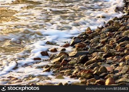 Small stones on the shore with the foam of the waves during tropical sunset. Small stones on the shore with the foam