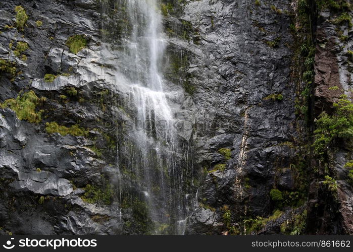 Small stream crashes on black rock wall in the depth