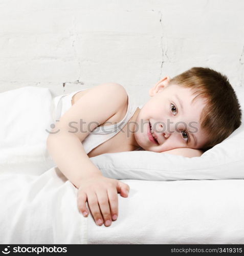 Small toddler boy (4 years old) is lying in bed and smiling. He is looking at the camera
