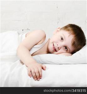 Small toddler boy (4 years old) is lying in bed and smiling. He is looking at the camera
